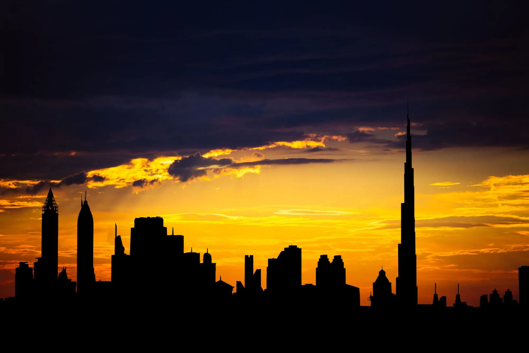 Silhouette of the Dubai skyline against an orange sunset